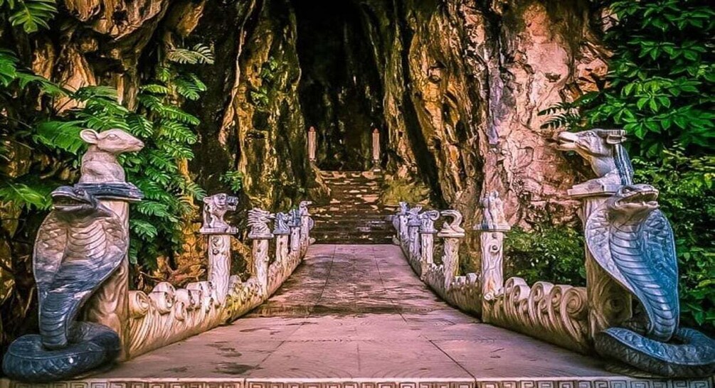 A pathway flanked by statues of mythical creatures leading into a cave. 3