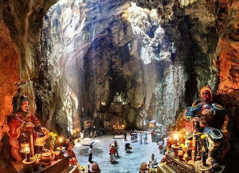 A cave interior with statues and artifacts, including a seated Buddha and a figure holding a scroll. 2