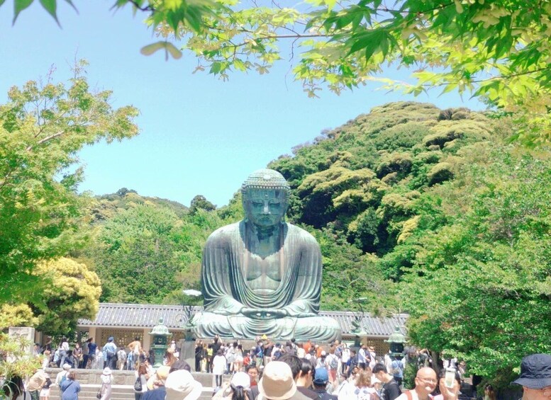 A large Buddha statue surrounded by lush greenery and a crowd of visitors. 1