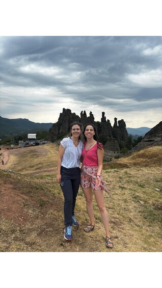 Two people standing in a grassy field with rocky formations in the background. 3