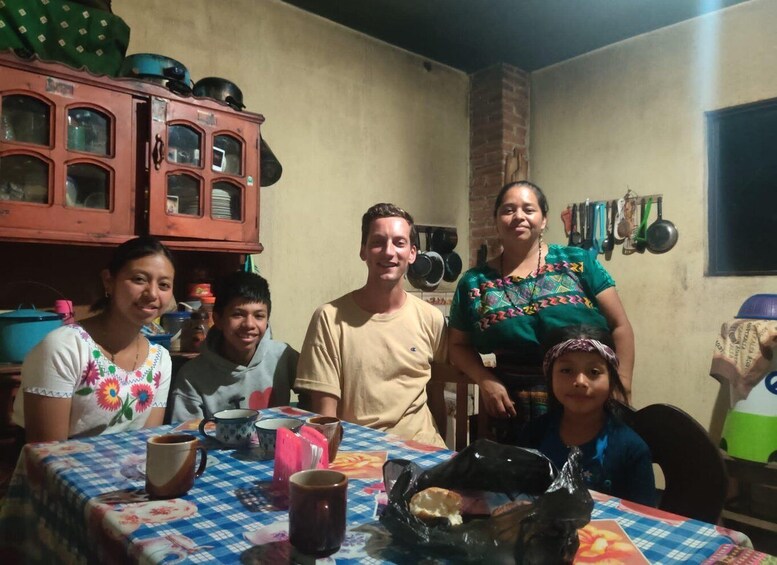 A family dining at a table with a colorful tablecloth, surrounded by kitchen cabinets and utensils. 1