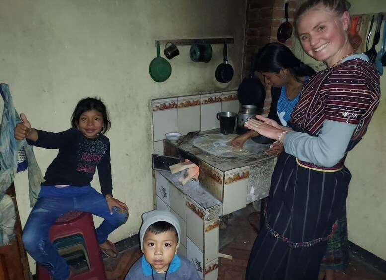 A kitchen with a woman cooking and two children, one on a stool and one on the floor. 3