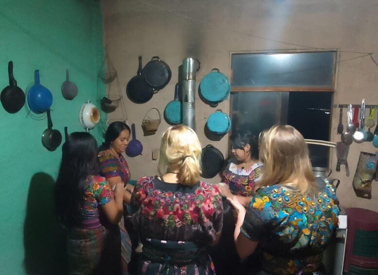 A group of women in colorful traditional attire standing in a kitchen with various pots and pans hanging on the wall. 5