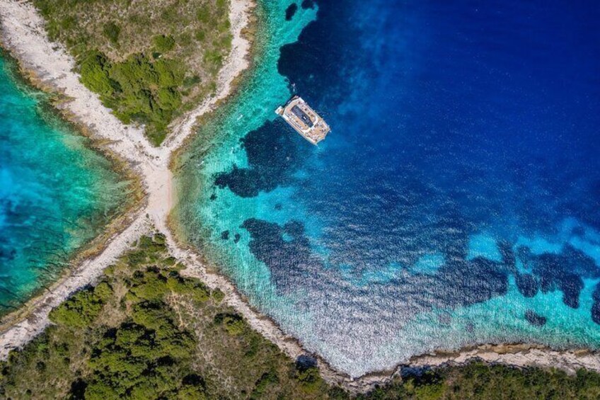 An aerial view of a coastal area with clear blue waters, a small boat, and a narrow strip of land with vegetation. 3