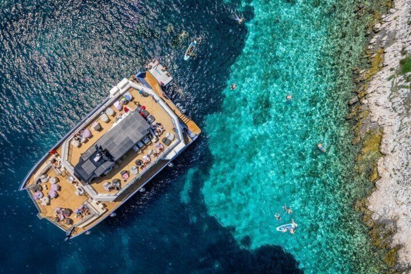 An aerial view of a boat with a deck area, surrounded by clear turquoise waters and a rocky coastline. 2