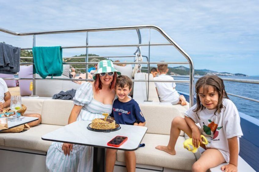 A boat with people sitting on the deck, a table with food, and a view of the sea. 5
