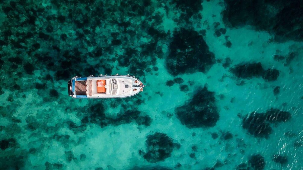 An aerial view of a boat on clear turquoise waters with coral formations. 1