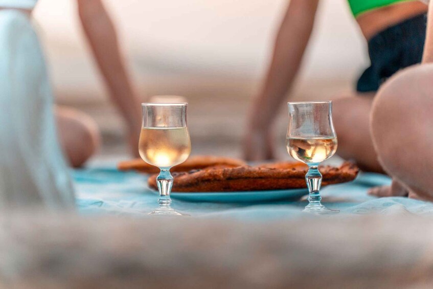 Two glasses of a clear liquid, possibly a beverage, on a blue surface with a plate of food in the background. 2