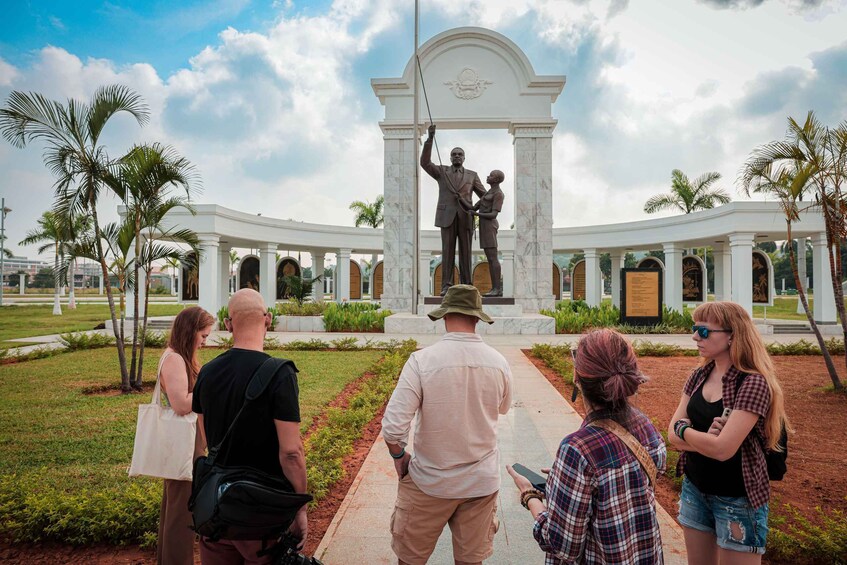 A group of people standing in front of a statue with a white archway. 3