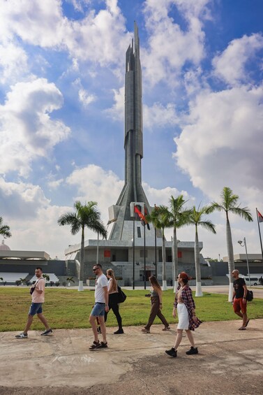 A tall, modern tower with palm trees and flags in a grassy area. 4