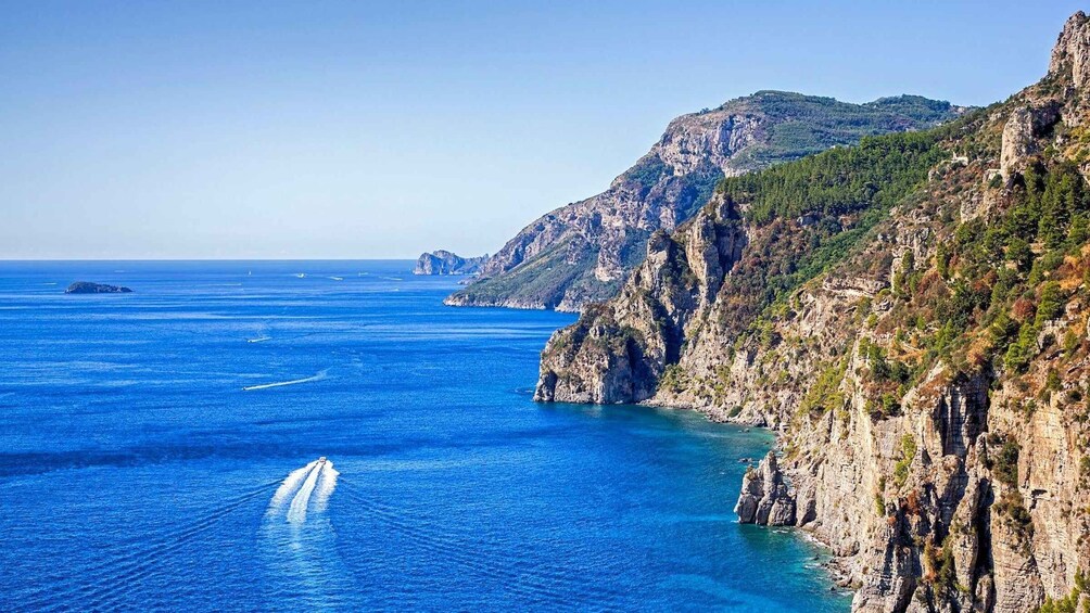 A coastal landscape with cliffs, clear blue sea, and a boat creating a wake. 5