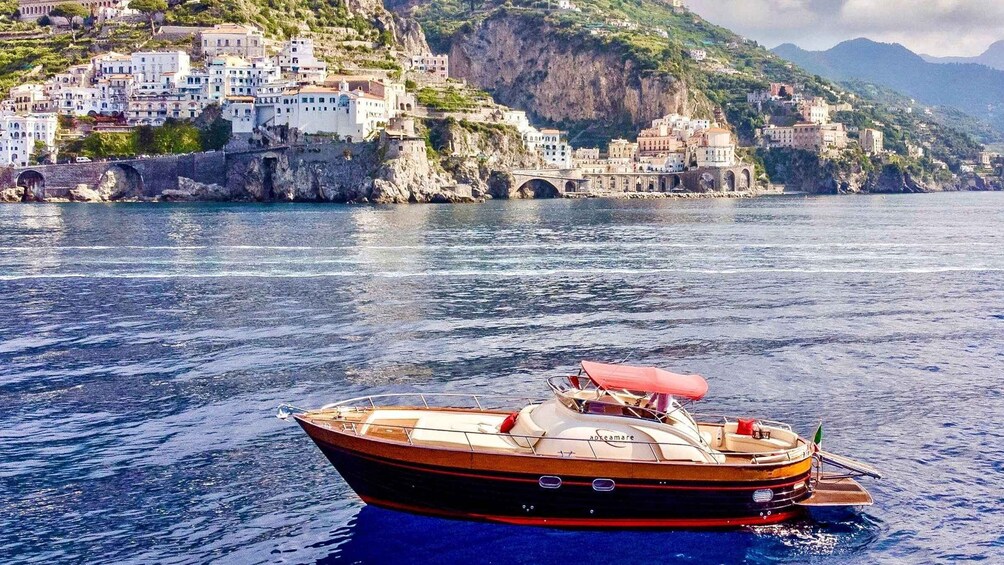 A boat named 'Adcamare' on calm waters with a coastal town and mountains in the background. 4