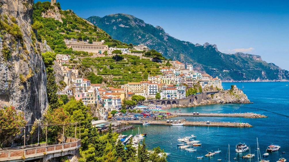A coastal town with colorful buildings, a marina, and mountains in the background. 1