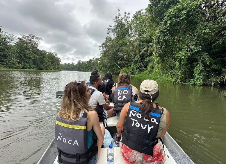 A group of people on a boat with 'NOCA' on their vests, navigating a river surrounded by dense greenery. 1