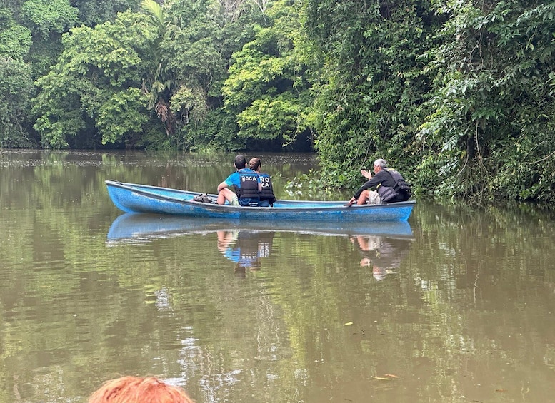 A blue canoe on calm water with three people wearing life jackets, surrounded by dense green foliage. 3