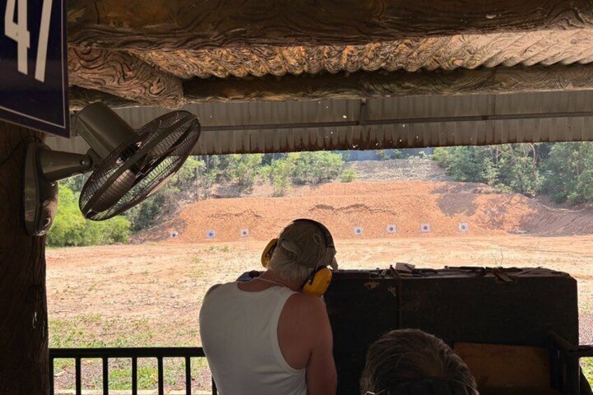 A person aiming at a target with a rifle, a fan, and a sign with the number 47. 4