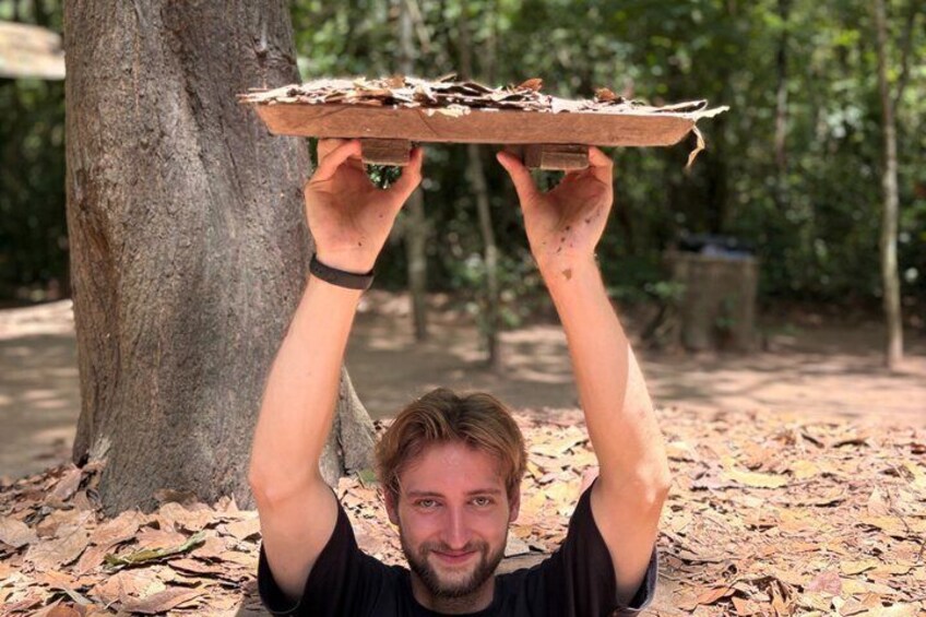 A person holding a flat, rectangular object with a rough texture, possibly a piece of wood, above their head outdoors. 1