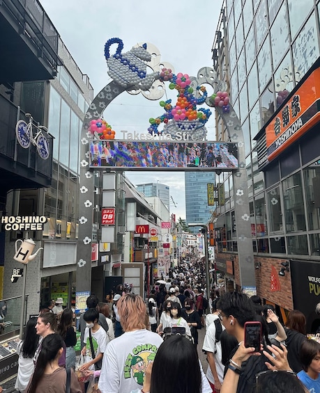 A bustling street scene with a crowd of people, a Takeshiba Street sign, and various storefronts including Hoshino Coffee. 1