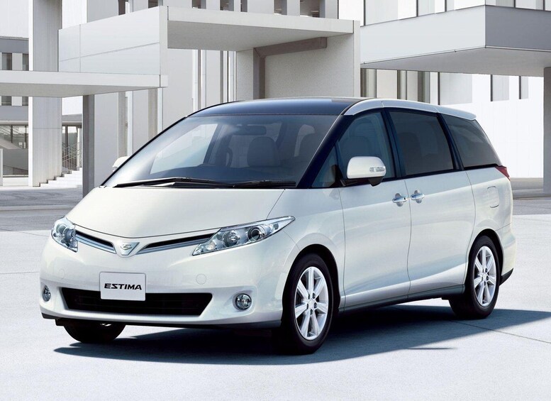 A white minivan parked in front of a modern building with large windows and a staircase. 3