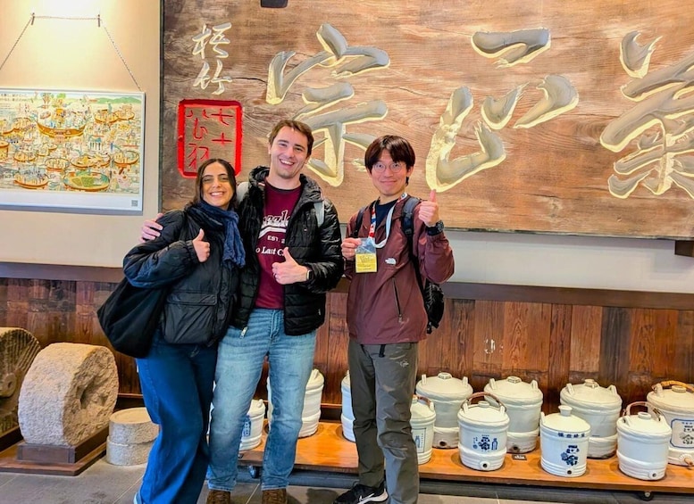 Three people standing in front of a wooden wall with Chinese calligraphy and a map. 1