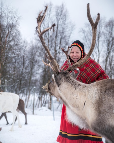 A person in a red plaid coat interacting with a reindeer in a snowy landscape. 1
