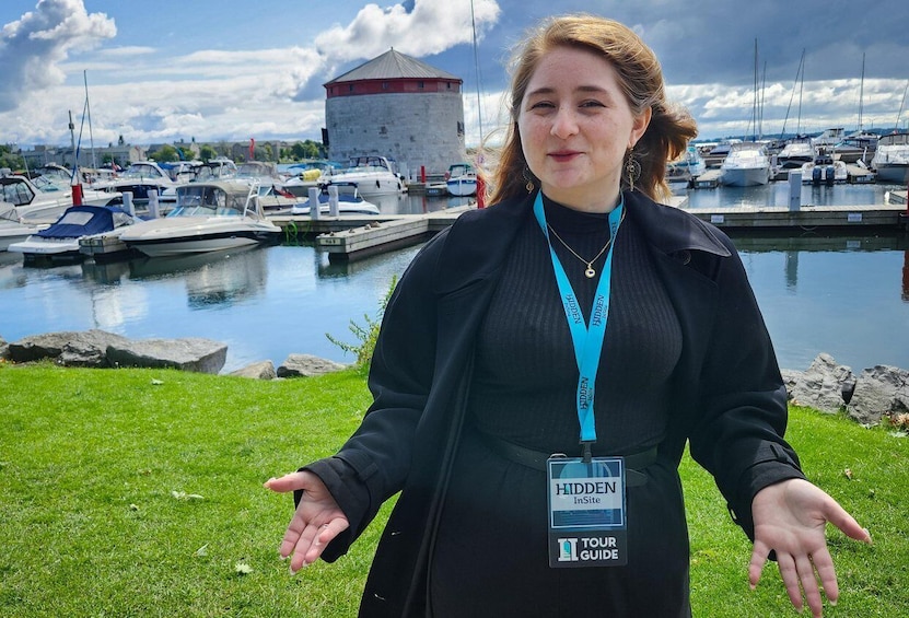A person standing on grass with a marina and a tower in the background. 1