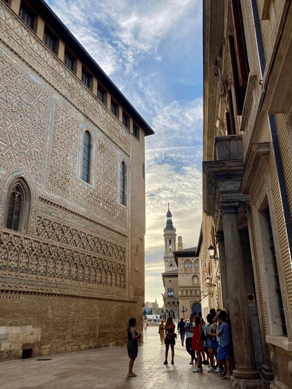 A historic building with intricate tile work, a clear sky, and a distant church spire. 4