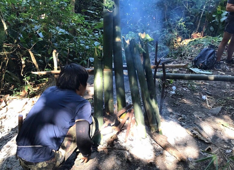 A person kneeling by a bamboo structure in a forested area. 4