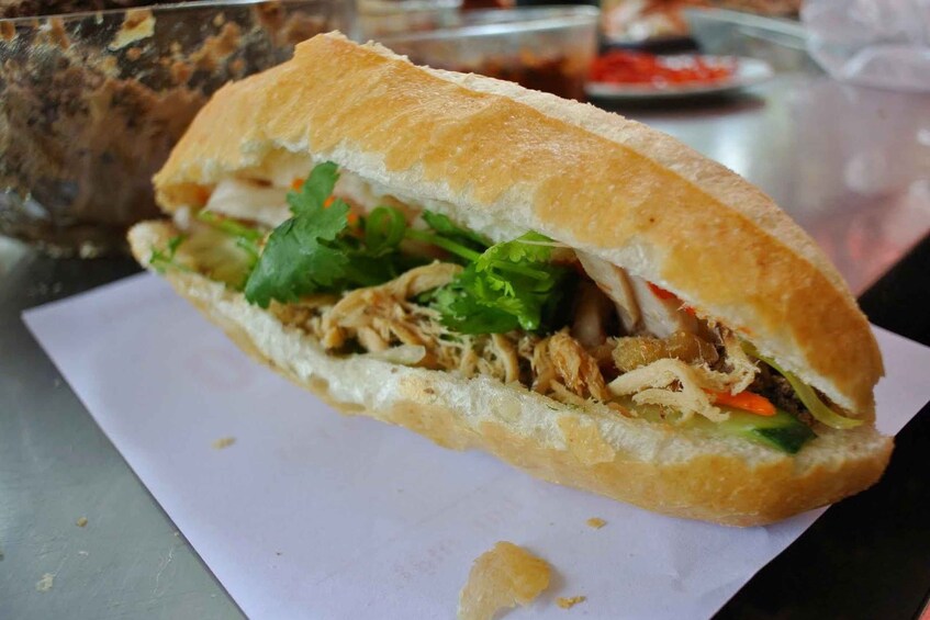 A sandwich with shredded meat, lettuce, and other vegetables on a white paper. 2