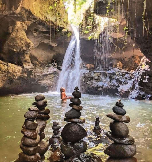 A waterfall, a person meditating, and stacks of stones in a natural setting. 3