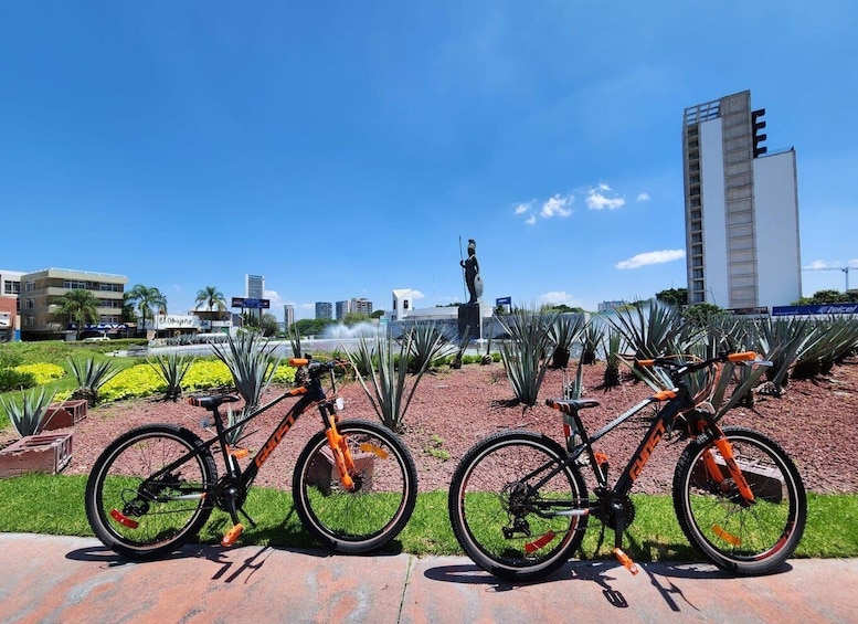 Two bicycles parked on a brick path with a statue and a tall building in the background. 5