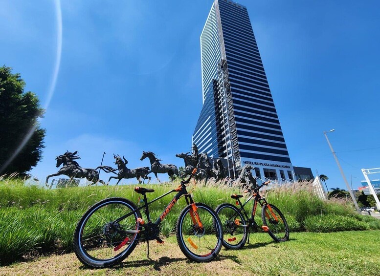 A statue of horses in motion, two bicycles, and a tall building labeled 'HOTEL RUI PLAZA GUADALARA' in the background. 1