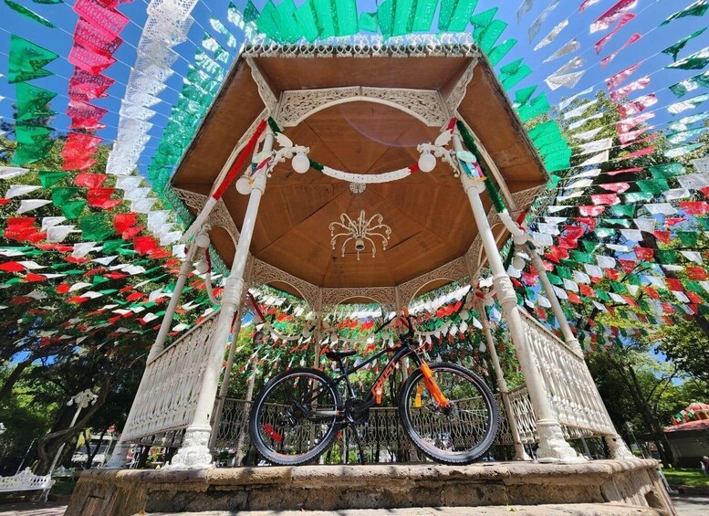 A gazebo with a bicycle parked underneath, surrounded by colorful flags. 2