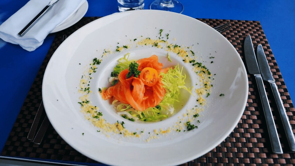 A white plate with a salad, garnished with shredded cheese and herbs, on a blue tablecloth. 1