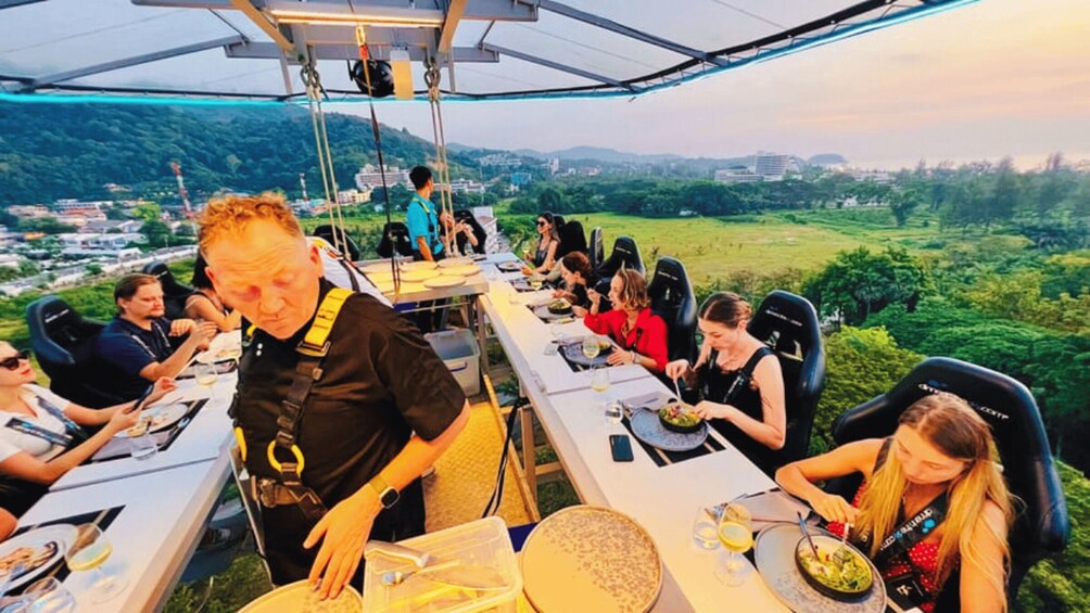 A group of people dining at a table with a scenic view of a hilly landscape. 4