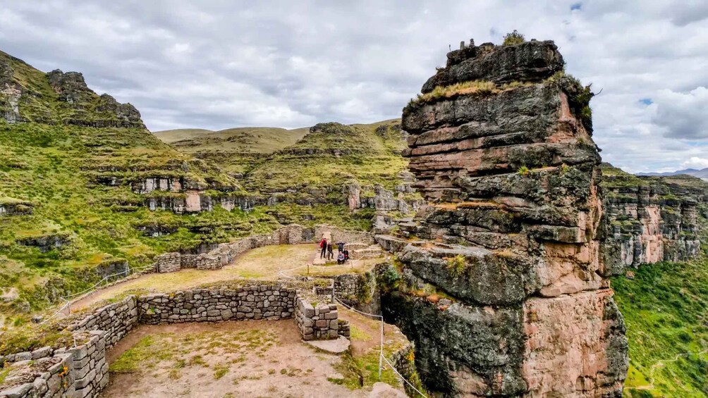 Ancient ruins with stone walls and a large rock formation in a mountainous landscape. 3