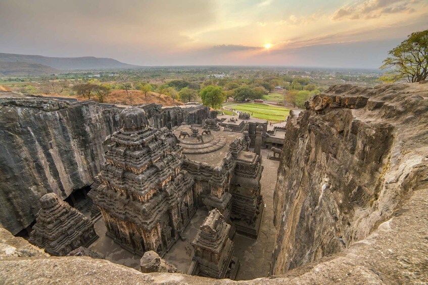 A historical temple complex carved into rock, with a view of a distant landscape and sunset. 2
