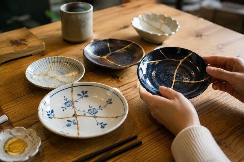 A wooden table with various ceramic dishes, including a blue and white floral plate and a dark blue bowl with a crack. 3