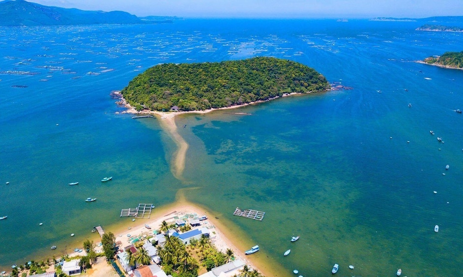 An island surrounded by clear blue waters with boats and a small beach area. 1
