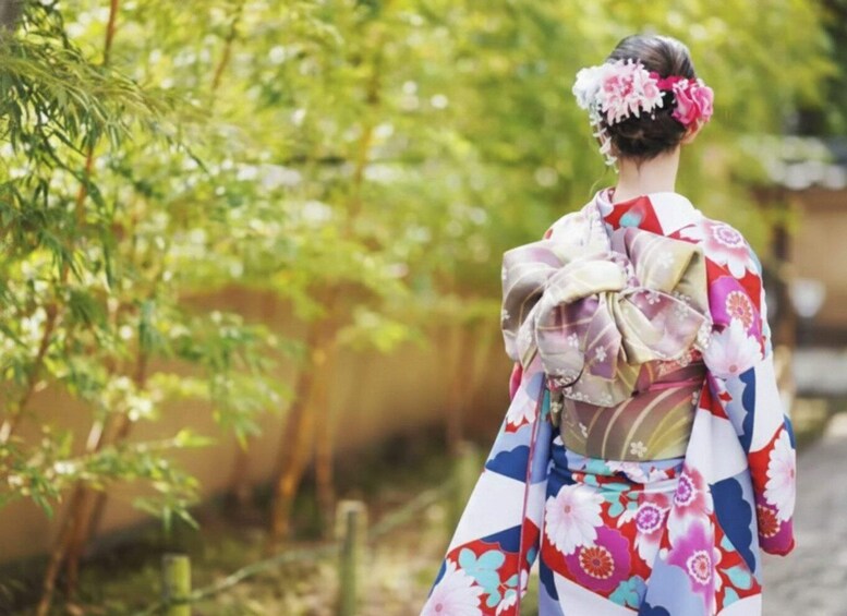 A person in a traditional Japanese kimono with floral patterns, walking through a garden with trees and a cobblestone path. 5