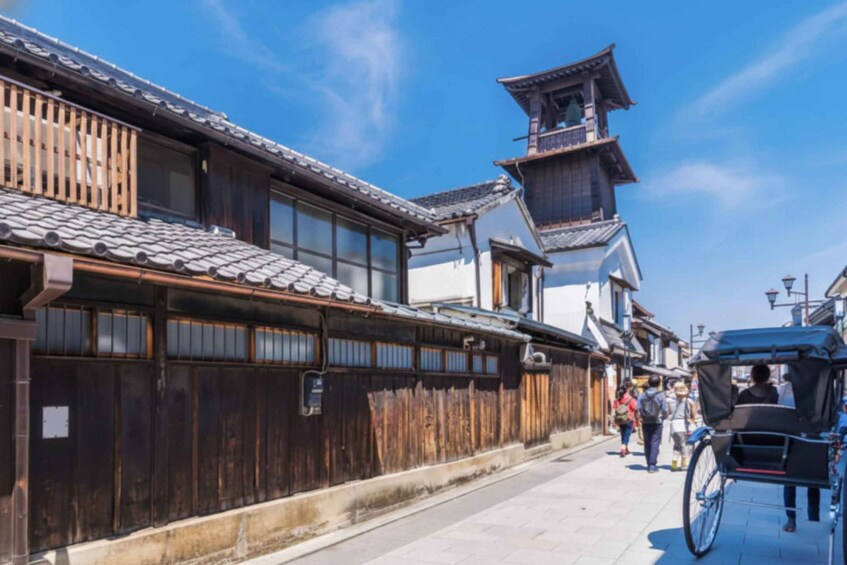 A traditional Japanese street with wooden fences, a rickshaw, and pedestrians. 1