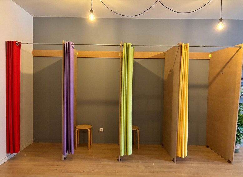 A room with four vertical curtains in red, purple, green, and yellow colors, wooden stools, and a plant. 5