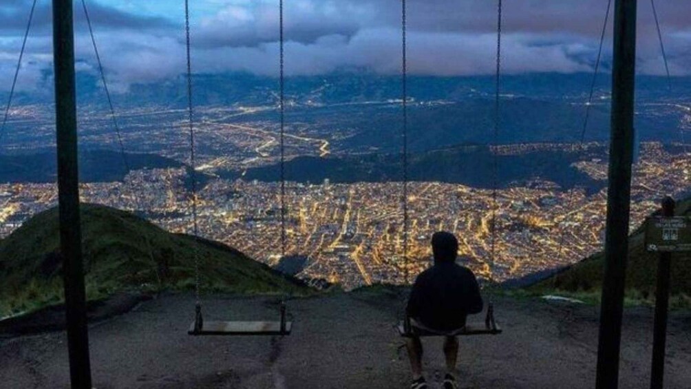 A person sitting on a swing overlooking a city at night. 2