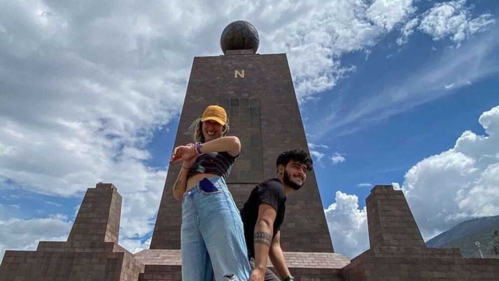 Two people dancing in front of a tall monument with a sphere on top and a letter 'N' on its side. 1