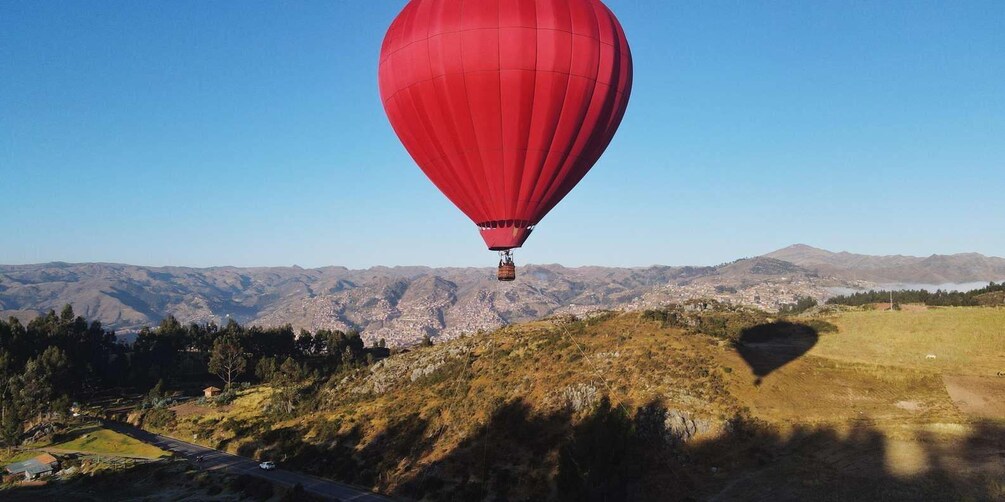 A red hot air balloon over a mountainous landscape with a town below. 1