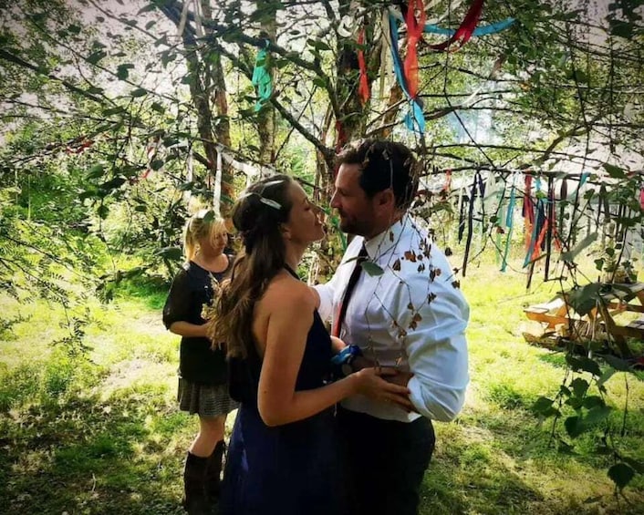 A couple embracing in a wooded area with greenery and hanging decorations. 1
