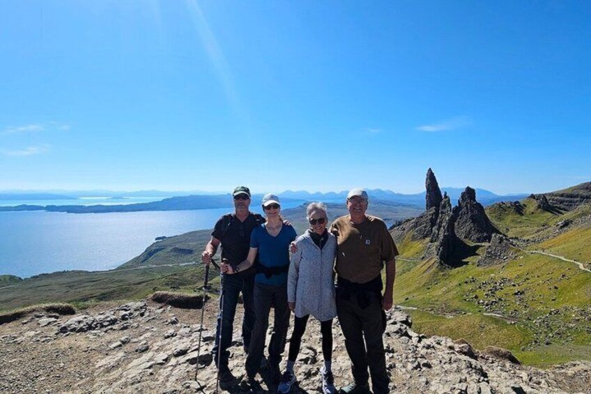 A group of people standing on a rocky outcrop with a view of a body of water and distant mountains. 1