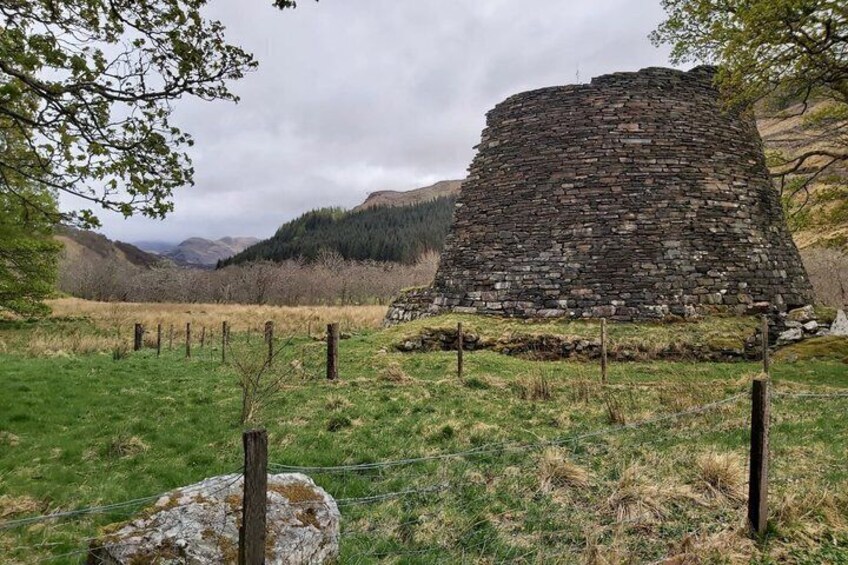 A stone structure in a rural landscape with a fence and a mountain in the background. 2