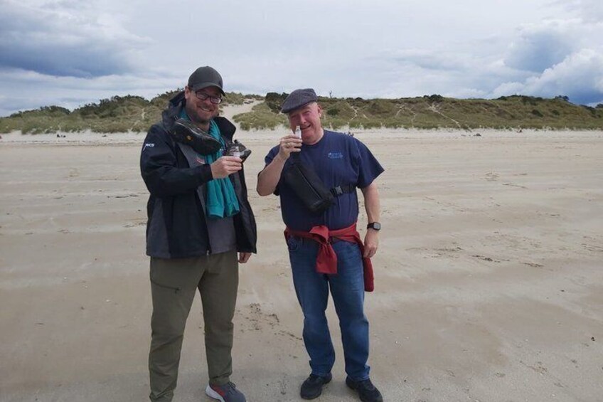 Two people standing on a sandy beach with dunes in the background. 5