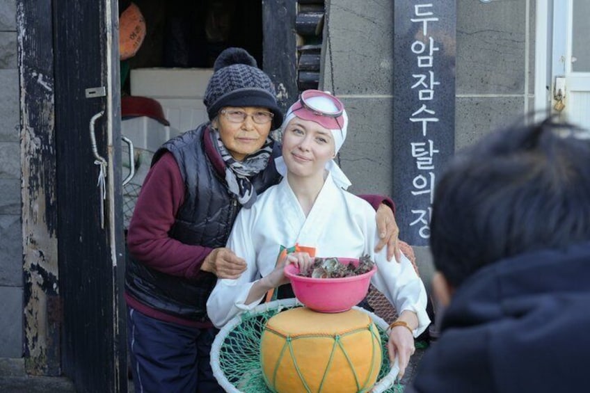 Two people outside a building with a sign in Korean. One person is holding a pink bowl with a plant. 3